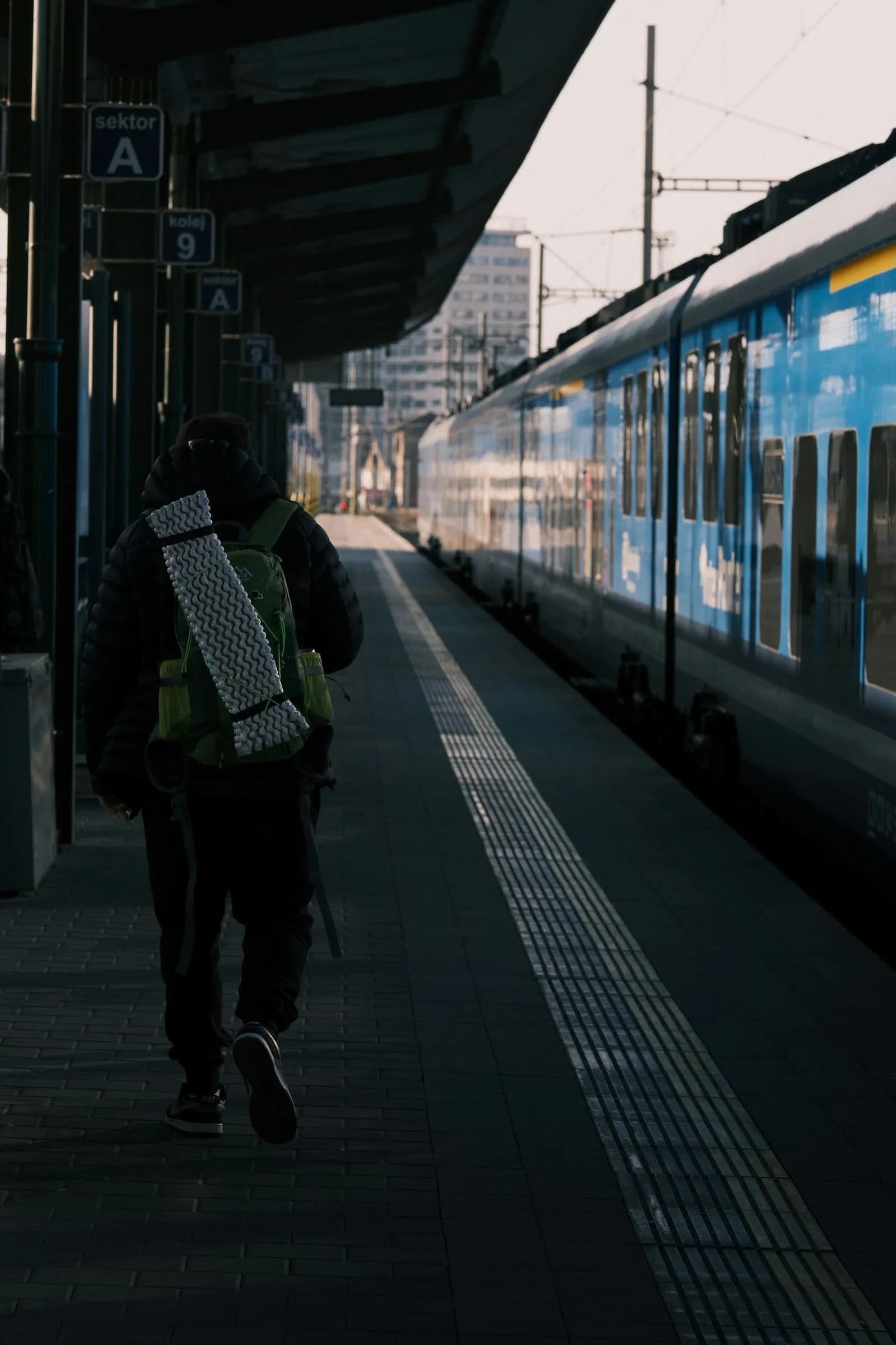 Sırt çantalı genç, tren peronunda yolculuğa yürüyor